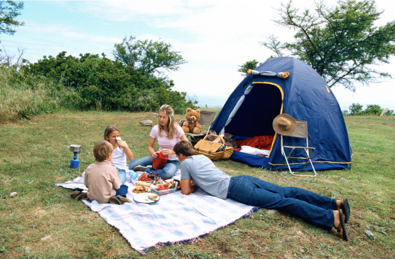 Family sitting on a blanket in front of a camping tent.