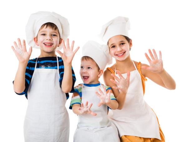 Three kids wearing chef's hats holding up their hands.