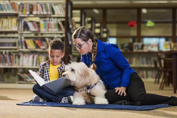 A child reading a book to an adult and a dog.