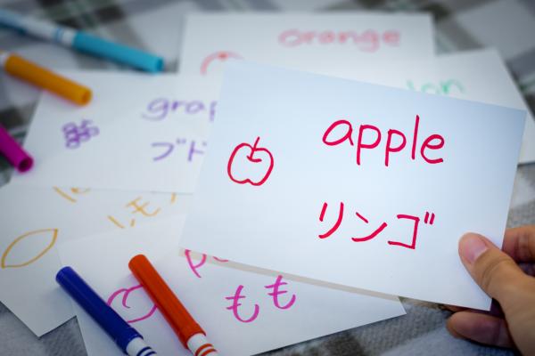 A picture of someone holding up a flash card with a drawing of an apple and the word apple written in both English and Japanese. 
