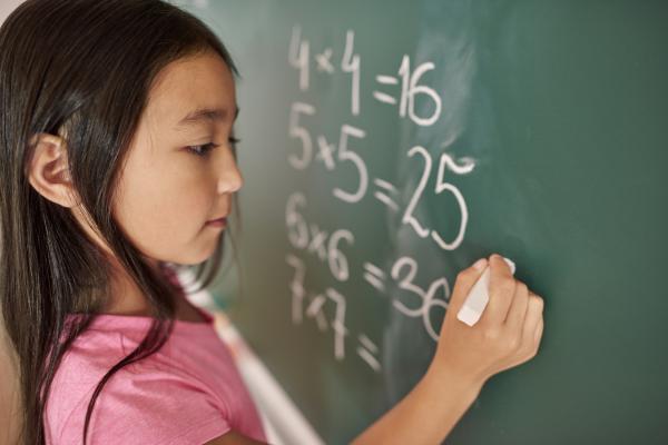 Young girl writing math equations with white chalk on a green chalkboard