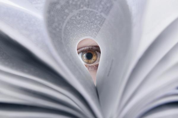 Open book with someone's eye peeking through the page.
