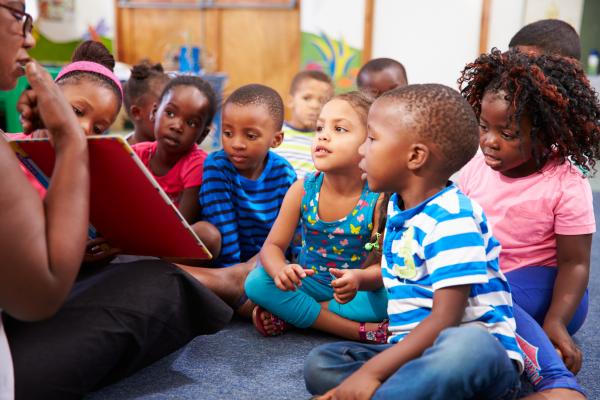 Toddlers sitting on the floor while an adult reads them a book.